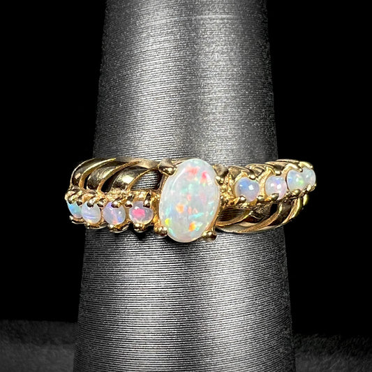 A yellow gold ring featuring two crossing, alternating lines of round cut Australian opals.  In the middle is a larger oval cut Australian opal.