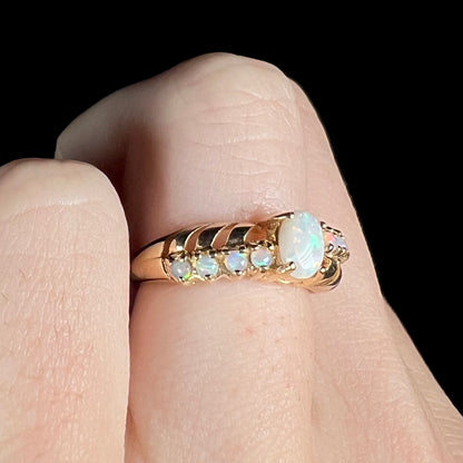 An Australian white opal crisscross ring in yellow gold, shown on a finger close-up from an angle.