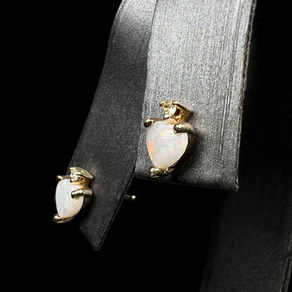 Angled close-up of a pair of Australian white opal heart and diamond earrings in 14k gold, shown on earring display.