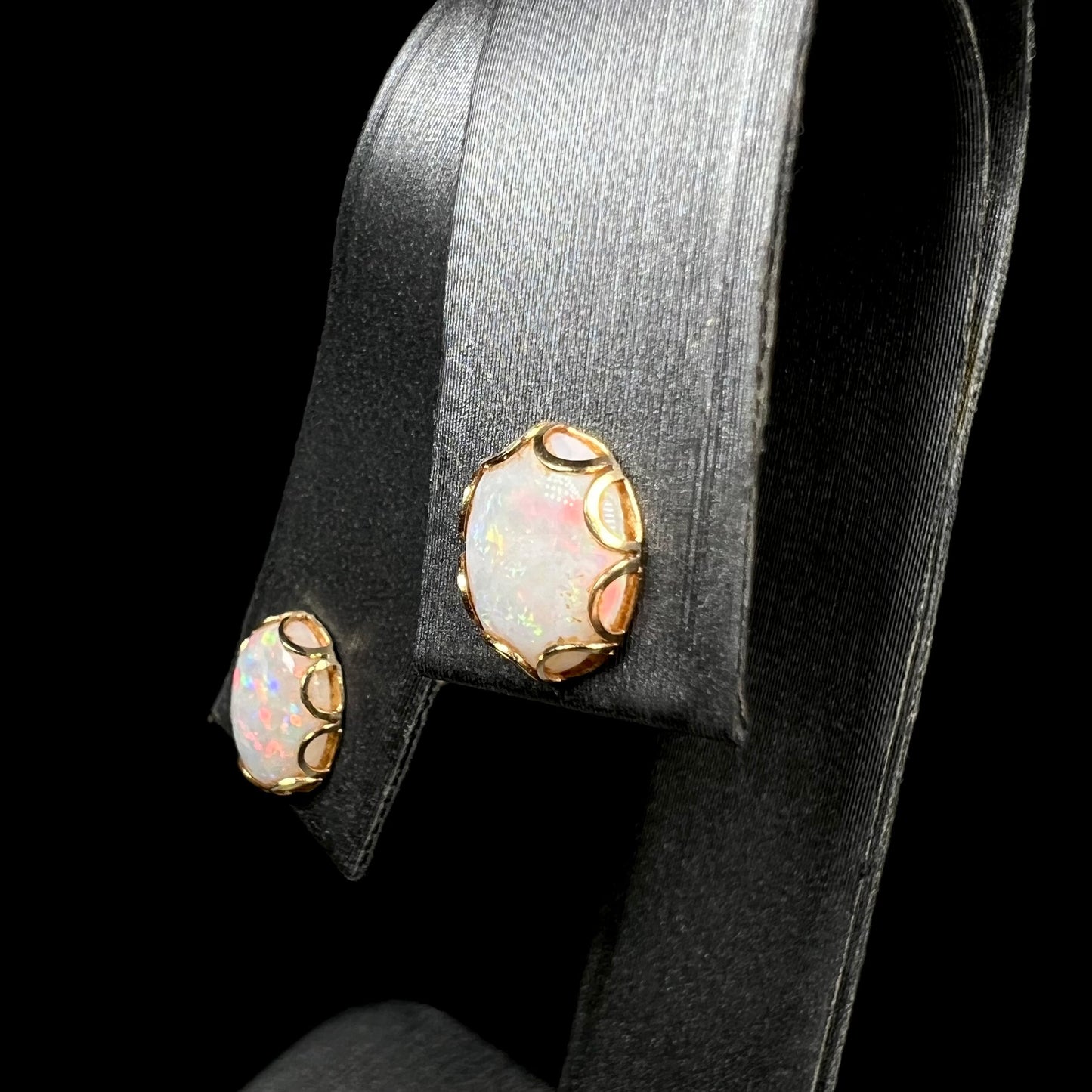 A pair of Australian white opal stud earrings in yellow gold shown from an angle on a ring display.