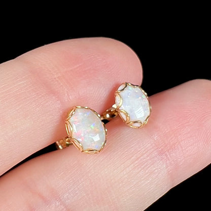 A pair of Australian white opal stud earrings in yellow gold shown close-up between two fingers from an angle.