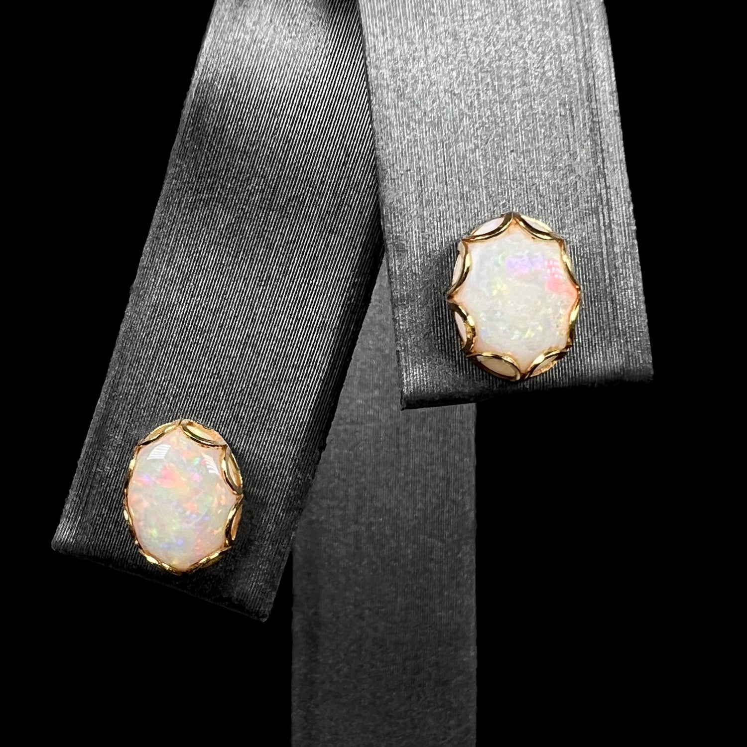 A pair of Australian white opal stud earrings in yellow gold shown close-up on a ring display.