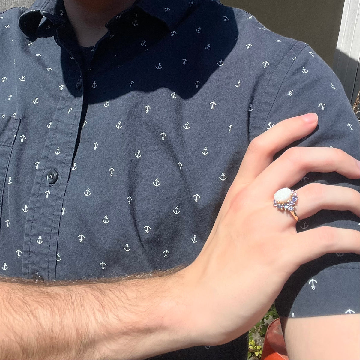 Sunlit close-up of person's hand resting on opposing shoulder wearing women's Australian white opal and tanzanite cluster ring