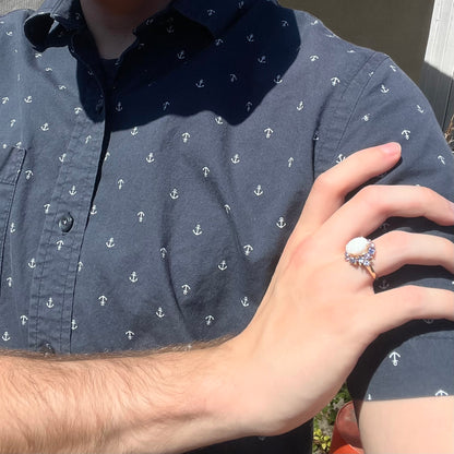 Sunlit close-up of person's hand resting on opposing shoulder wearing women's Australian white opal and tanzanite cluster ring