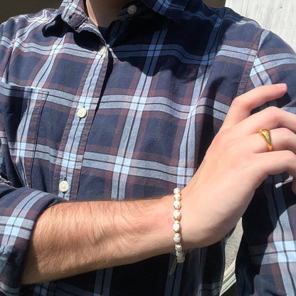 Hand resting on person's shoulder wearing blue plaid shirt, gold ring, and an Australian white opal tennis bracelet.