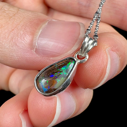 A natural, pear shaped Australian boulder opal with blue, purple, and green colors bezel set into a sterling silver necklace.