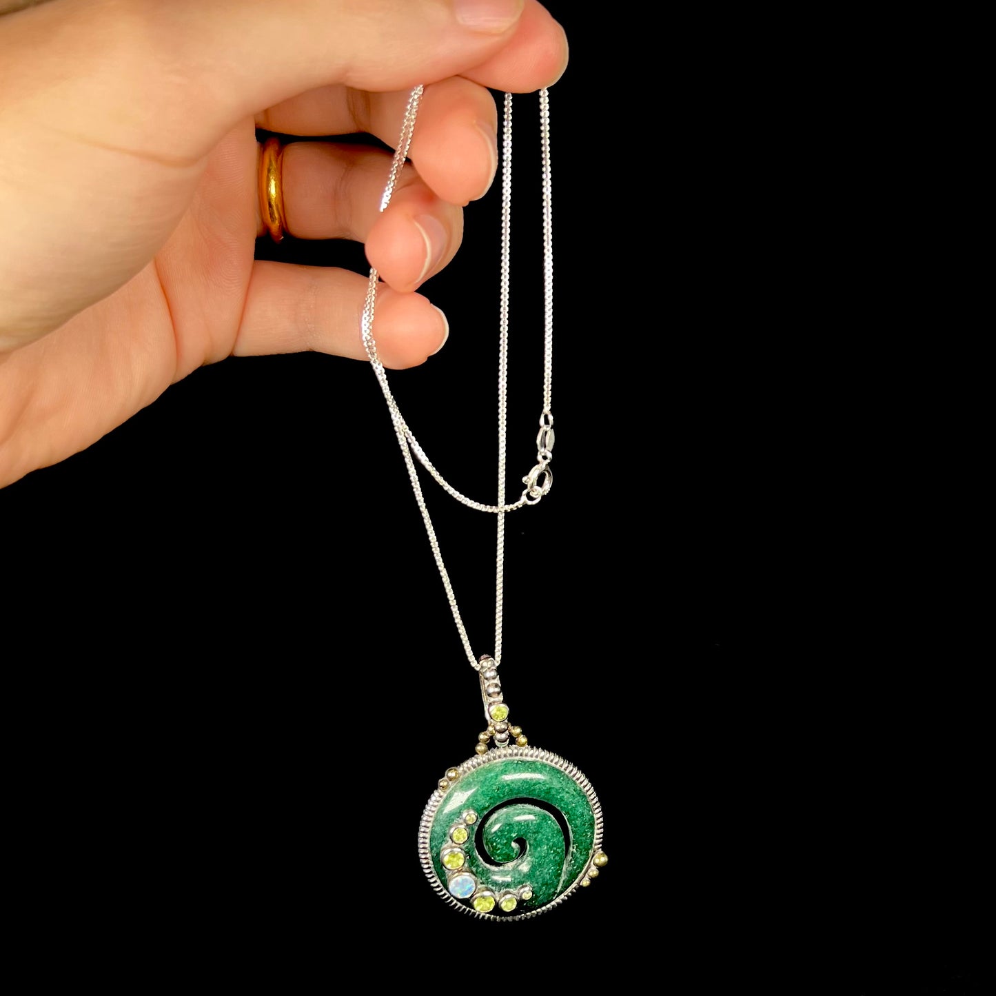 A men's carved green aventurine koru spiral pendant with peridot and opal accents, dangled by its chain.