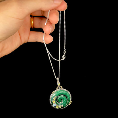 A men's carved green aventurine koru spiral pendant with peridot and opal accents, dangled by its chain.