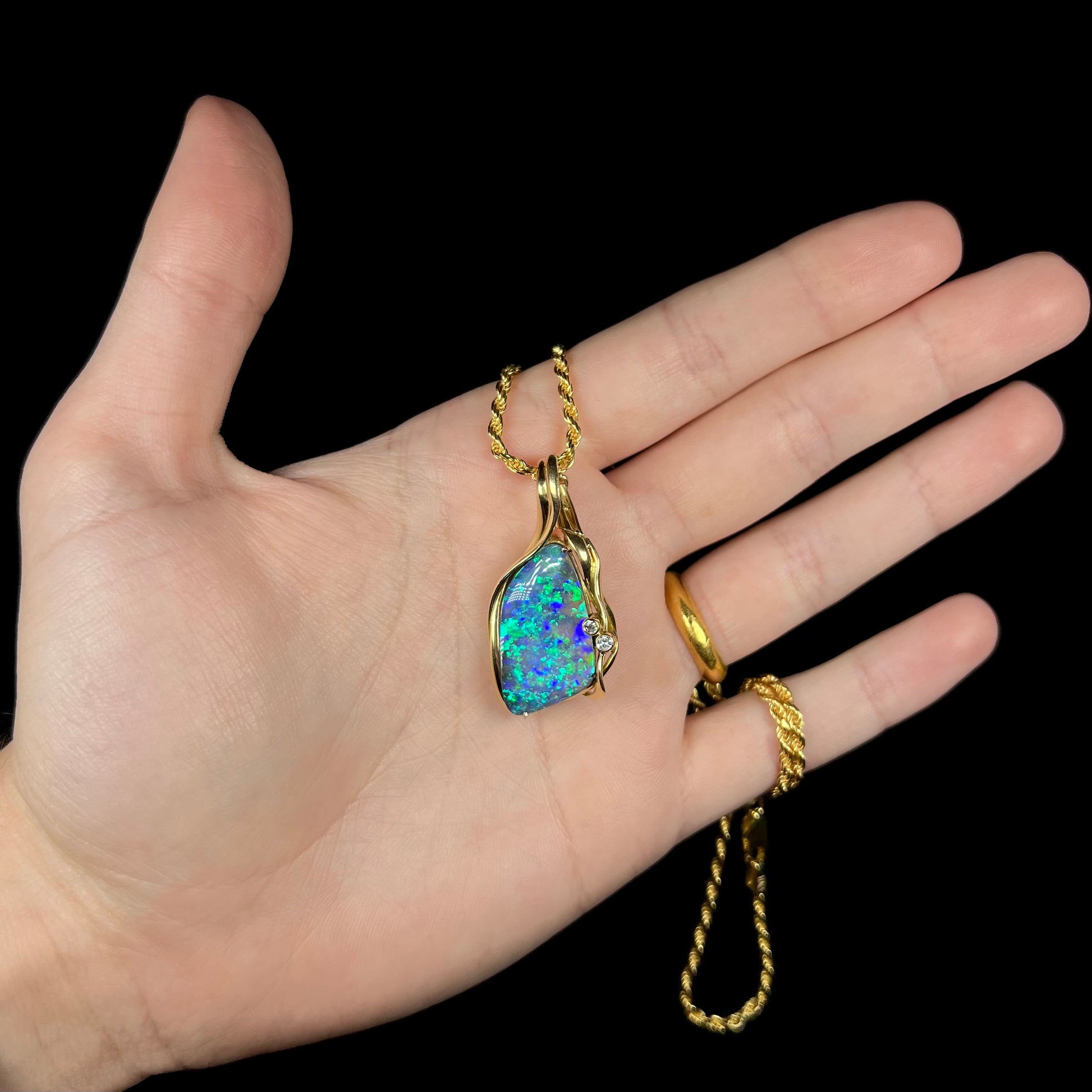 Hand holding a blue-green Australian boulder opal pendant with non-directional B5 brightness grade.