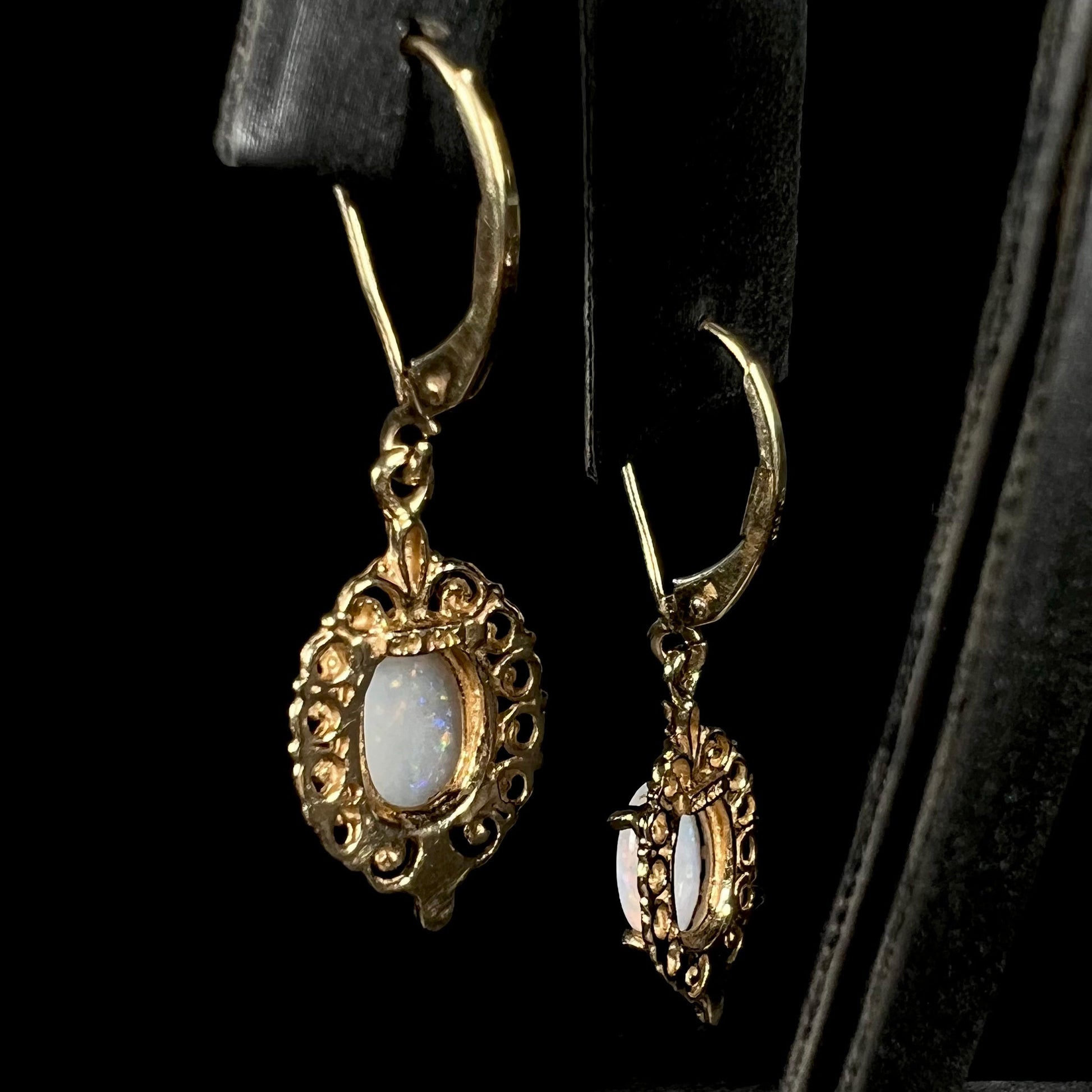 Back view of a pair of vintage yellow gold Australian light opal dangle earrings shown on an earring display.