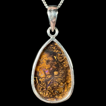 Back side of a pear shaped Koroit boulder opal pendant in sterling silver, shown against a black background.