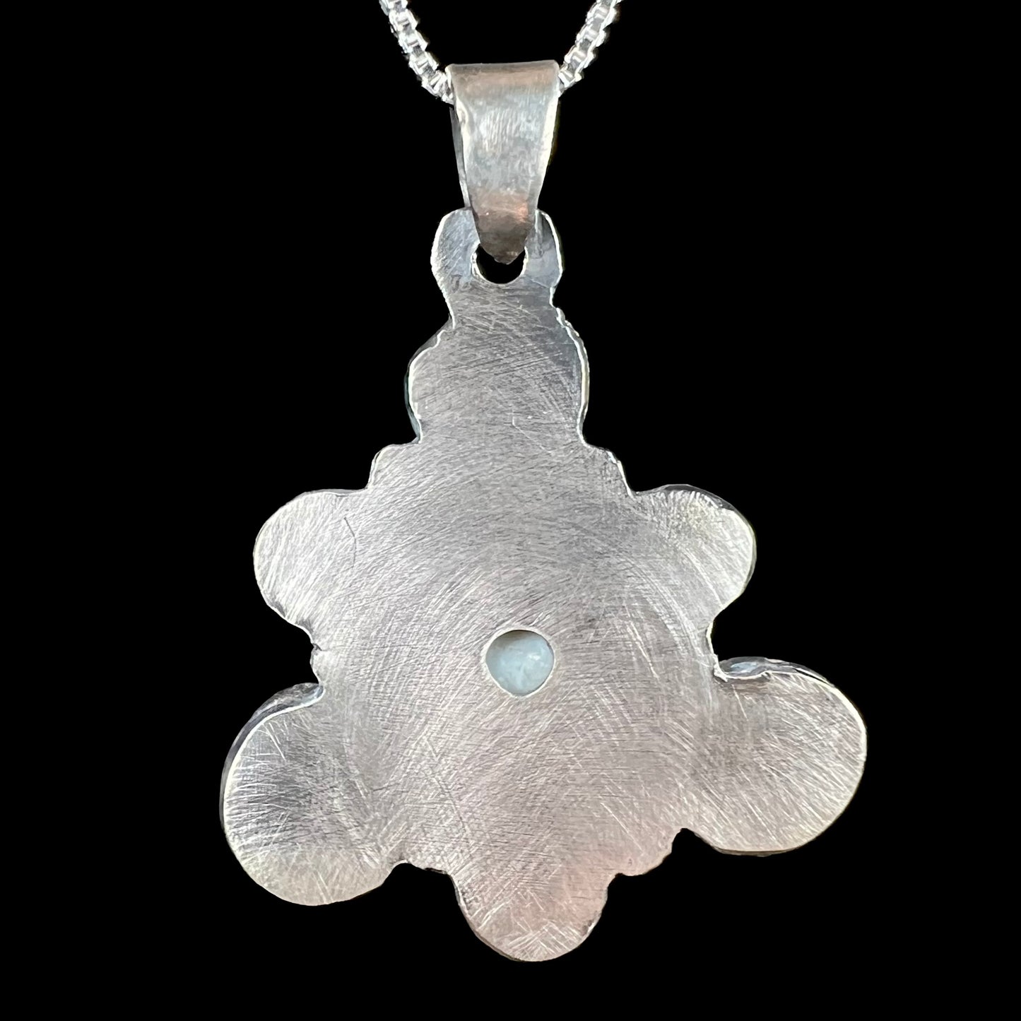 Back side of a rustic, handmade men's sterling silver opal pendant, shown against a black background.