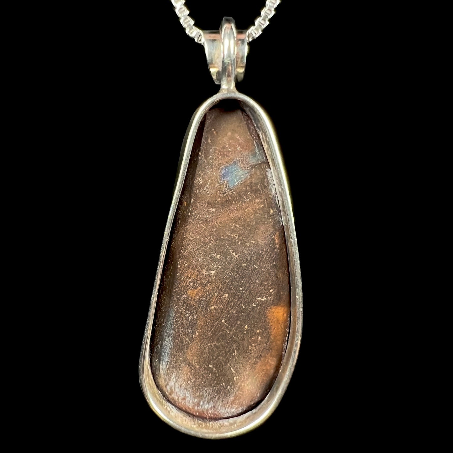 Back side of an eggplant-shaped sterling silver boulder opal pendant, shown against a black background.