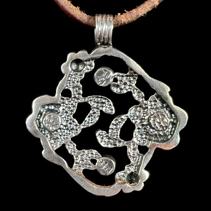 Back of a sterling silver pendant stamped "925", "14k", and "B. IL." on a brown cord against a black background.