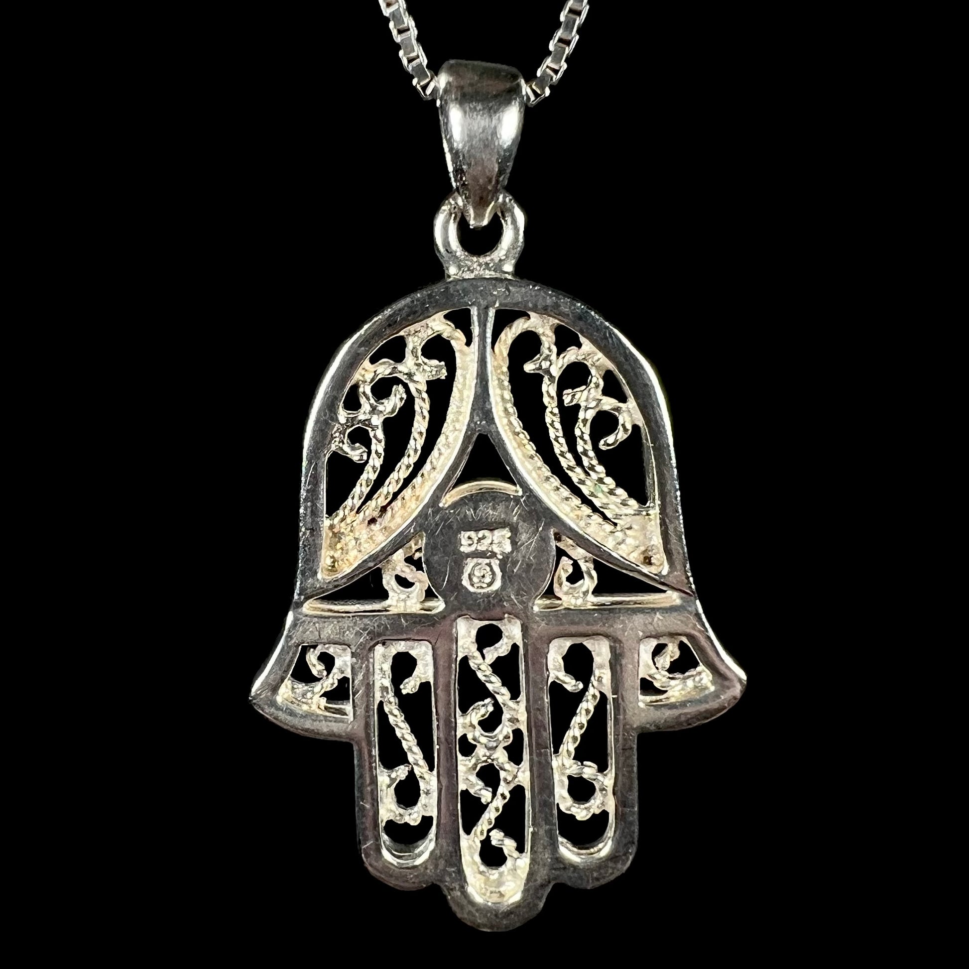 Back of A sterling silver and filigree-accented hamsa hand necklace against a black background.