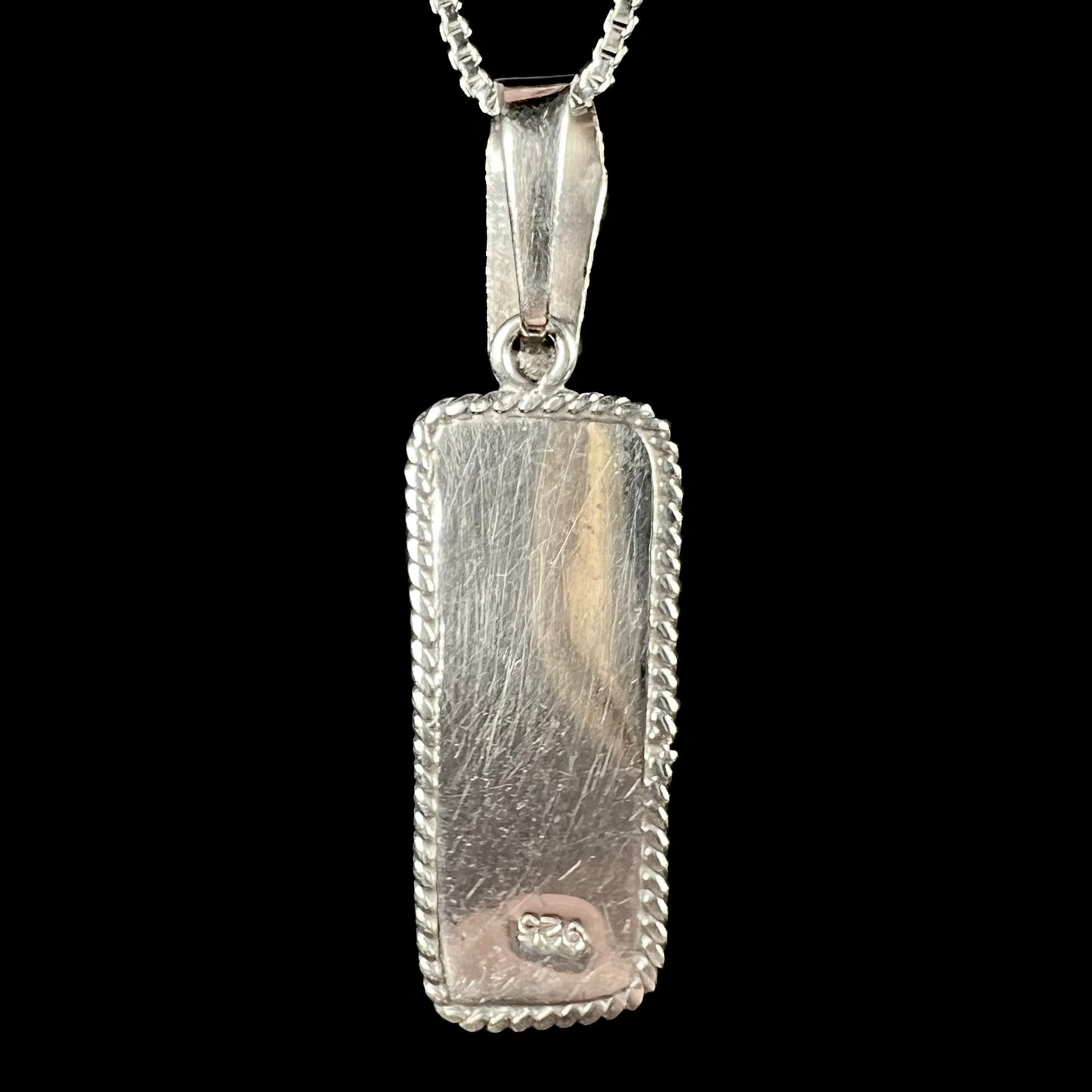 Back side of a sterling silver pendant, shown against a black background.