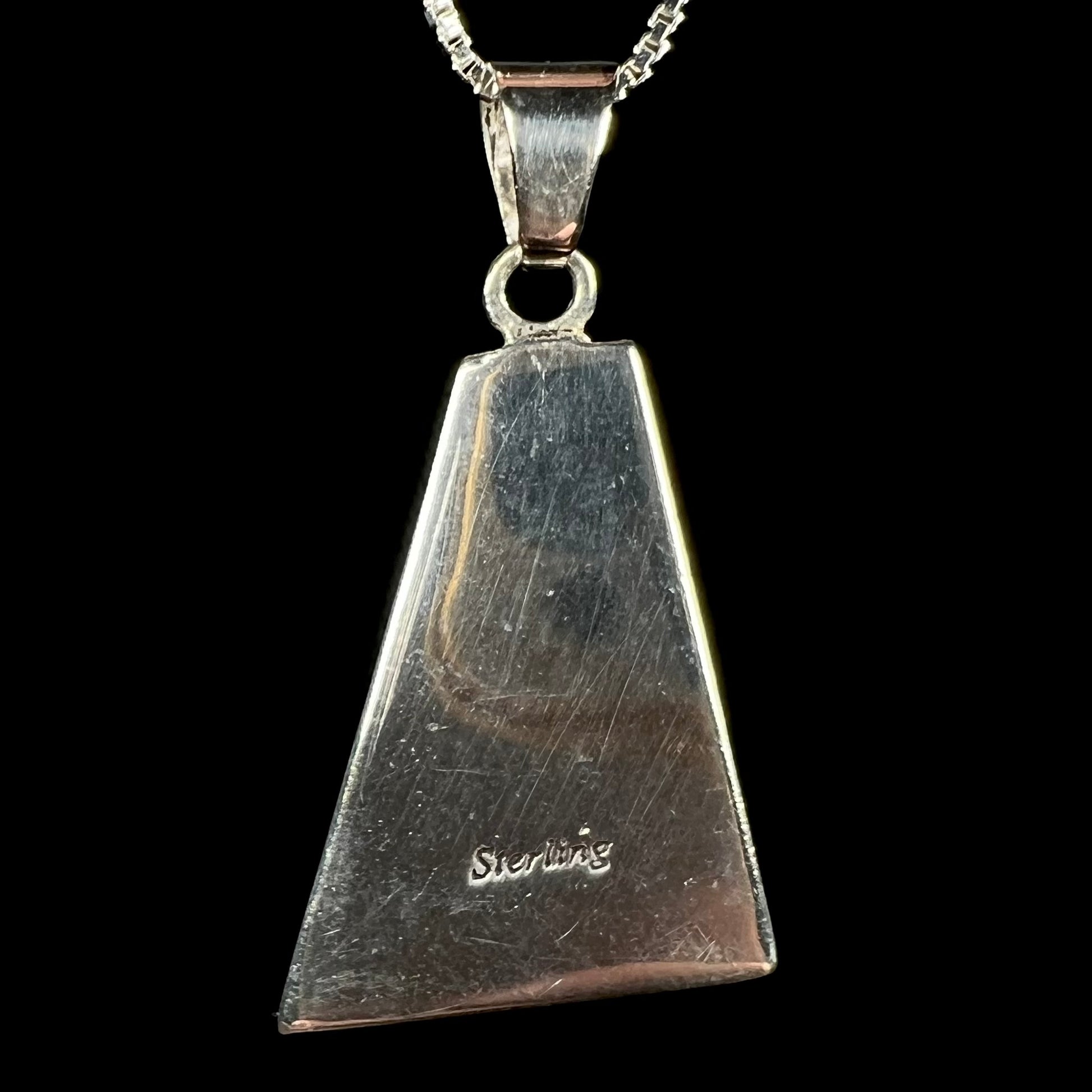 The back of a sterling silver pendant shown close-up against a black background.