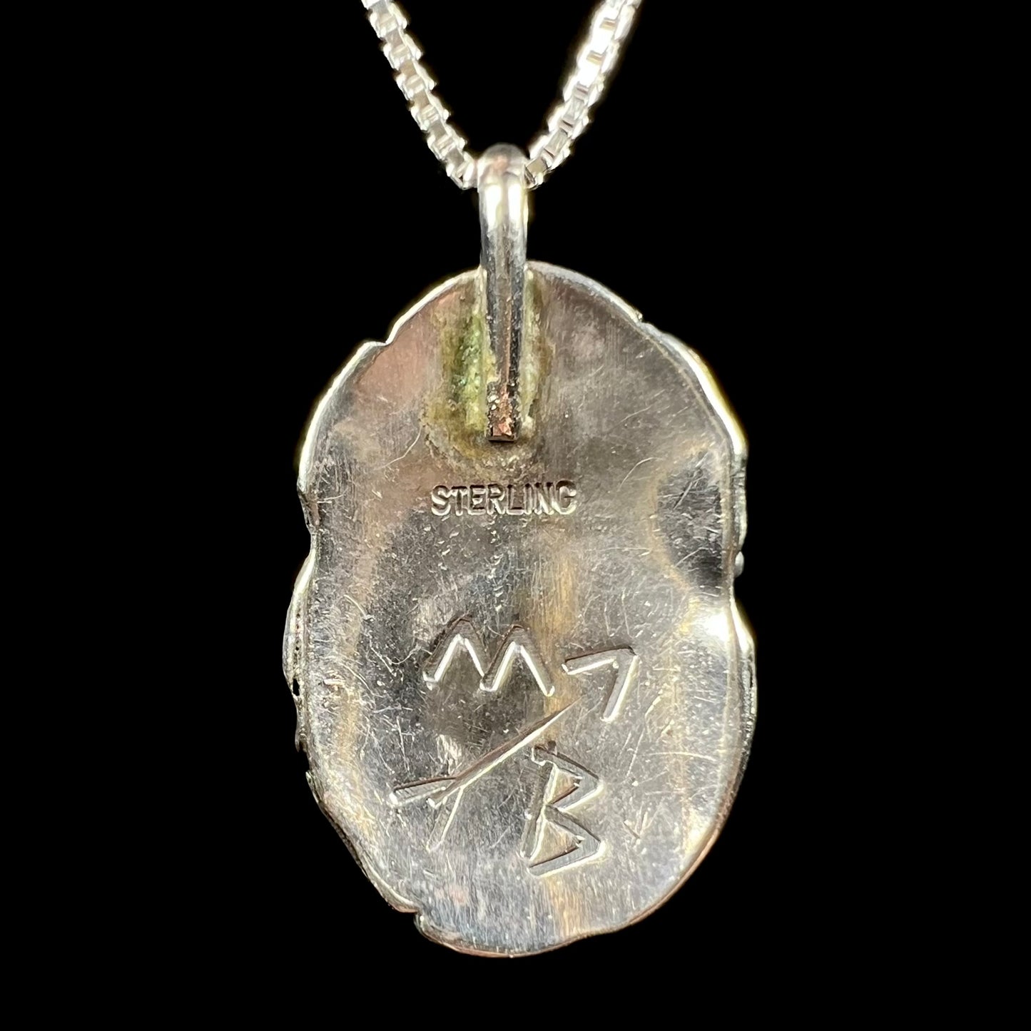 Back of a Southwest-style sterling silver pendant signed "MB", with the letters separated by an arrow.