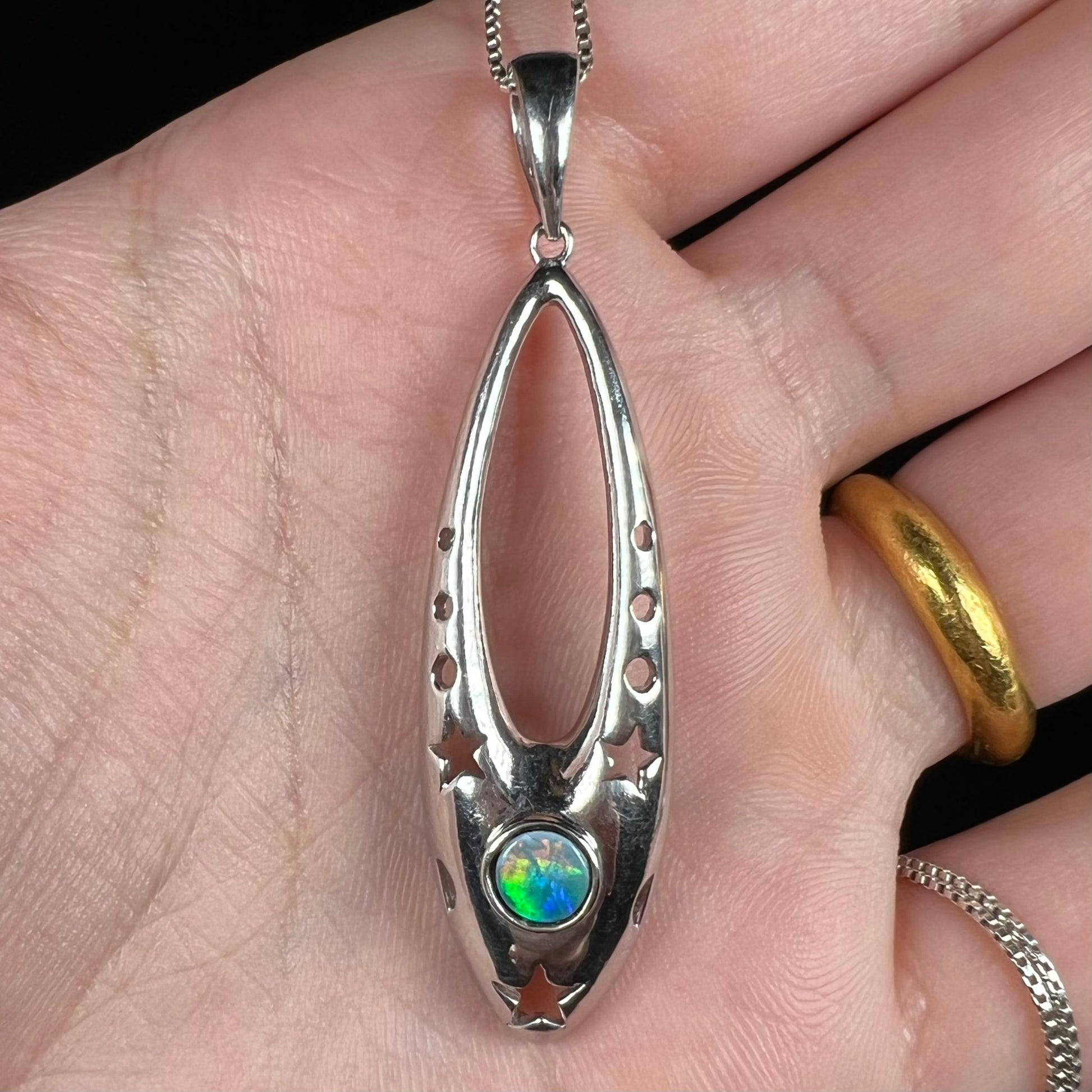 Close-up of a sterling silver and opal doublet ballerina shoe necklace shown in a hand.