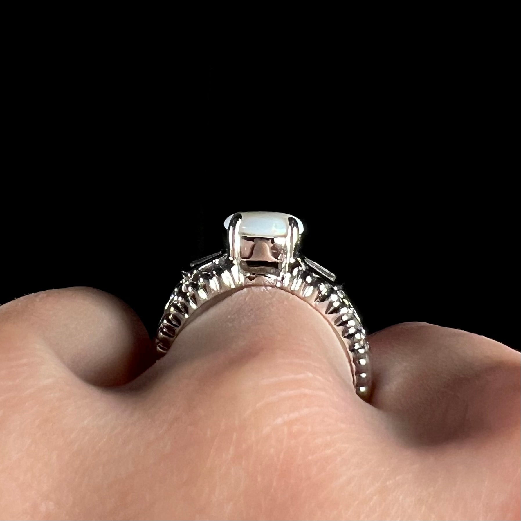 Side gallery profile view of a round Australian white opal and CZ ring in white base metal.