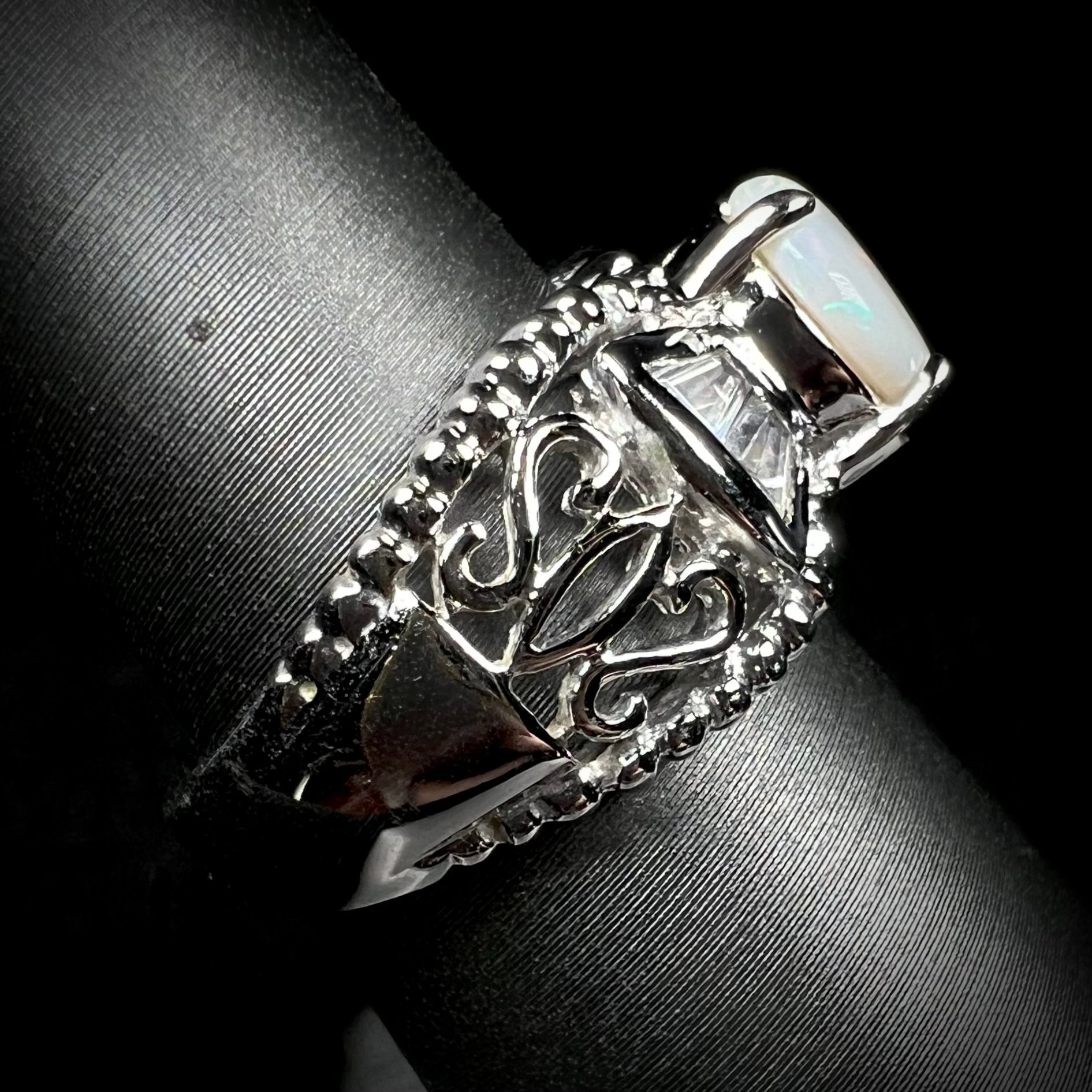 Side shank view of a round Australian white opal and CZ ring in white base metal.