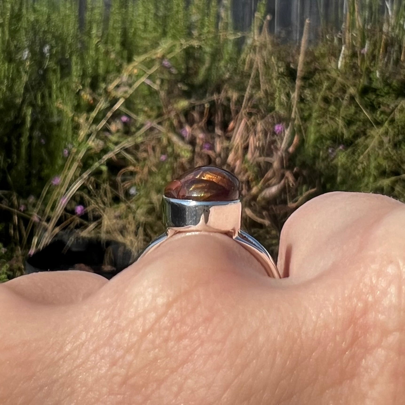 Side gallery view of a bezel set fire agate ring worn on a hand in the sunlight.