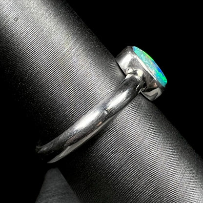 Side view of bezel set opal solitaire ring on ring display, focusing on ring's silver shank