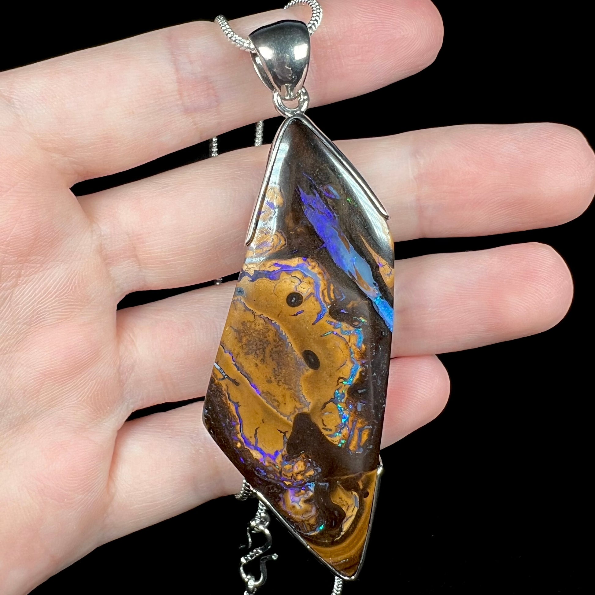 Close-up of big Australian boulder opal men's pendant with freeform shape, held in hand