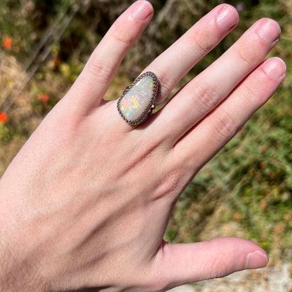 A big Australian opal cocktail ring in sterling silver, worn on a hand in natural sunlight.  The opal has soft orange flashes of color.