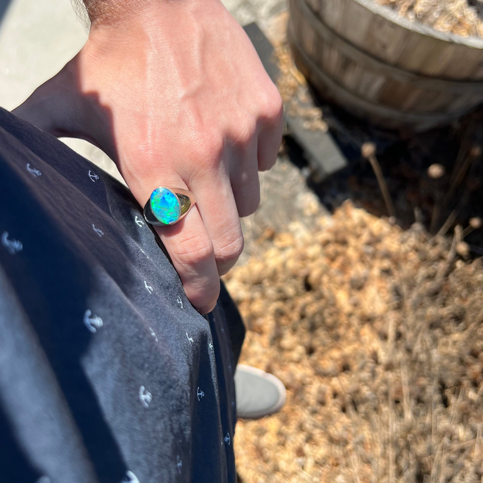 Hand resting on person's hip while wearing a big blue Australian opal men's ring in sunlight