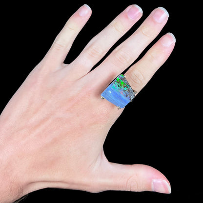 A hand wearing a big boulder opal ring with green flashes seen in the opal's ironstone matrix.