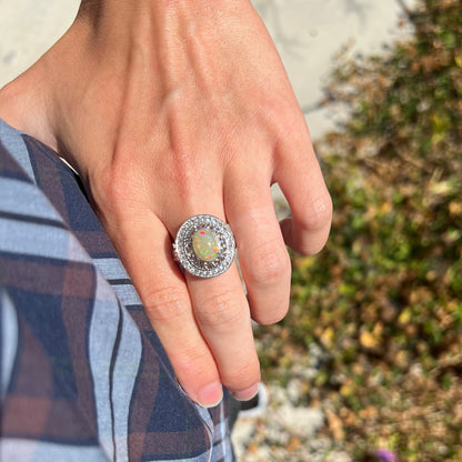 A big opal ring worn on a hand resting on a hip in the sunlight.