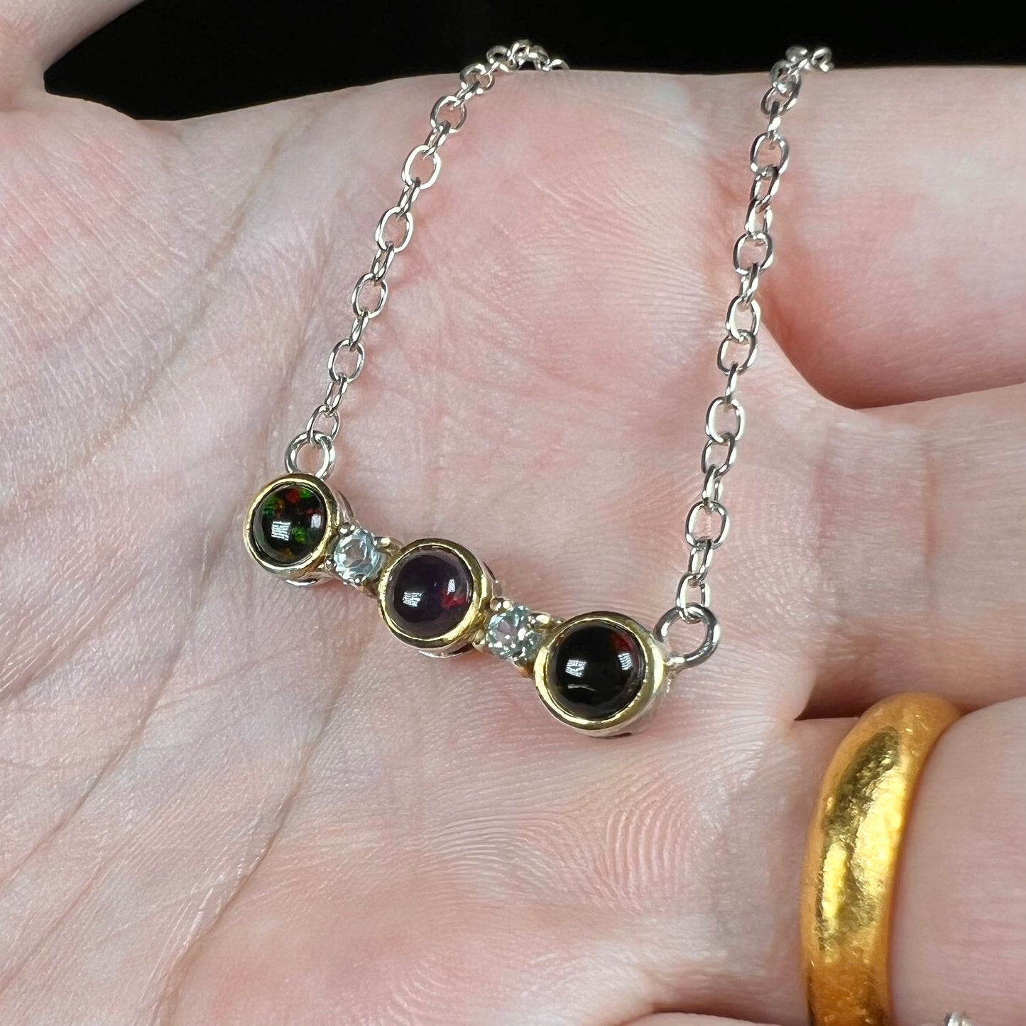A three-stone black Ethiopian opal and white topaz necklace in two-tone sterling silver.