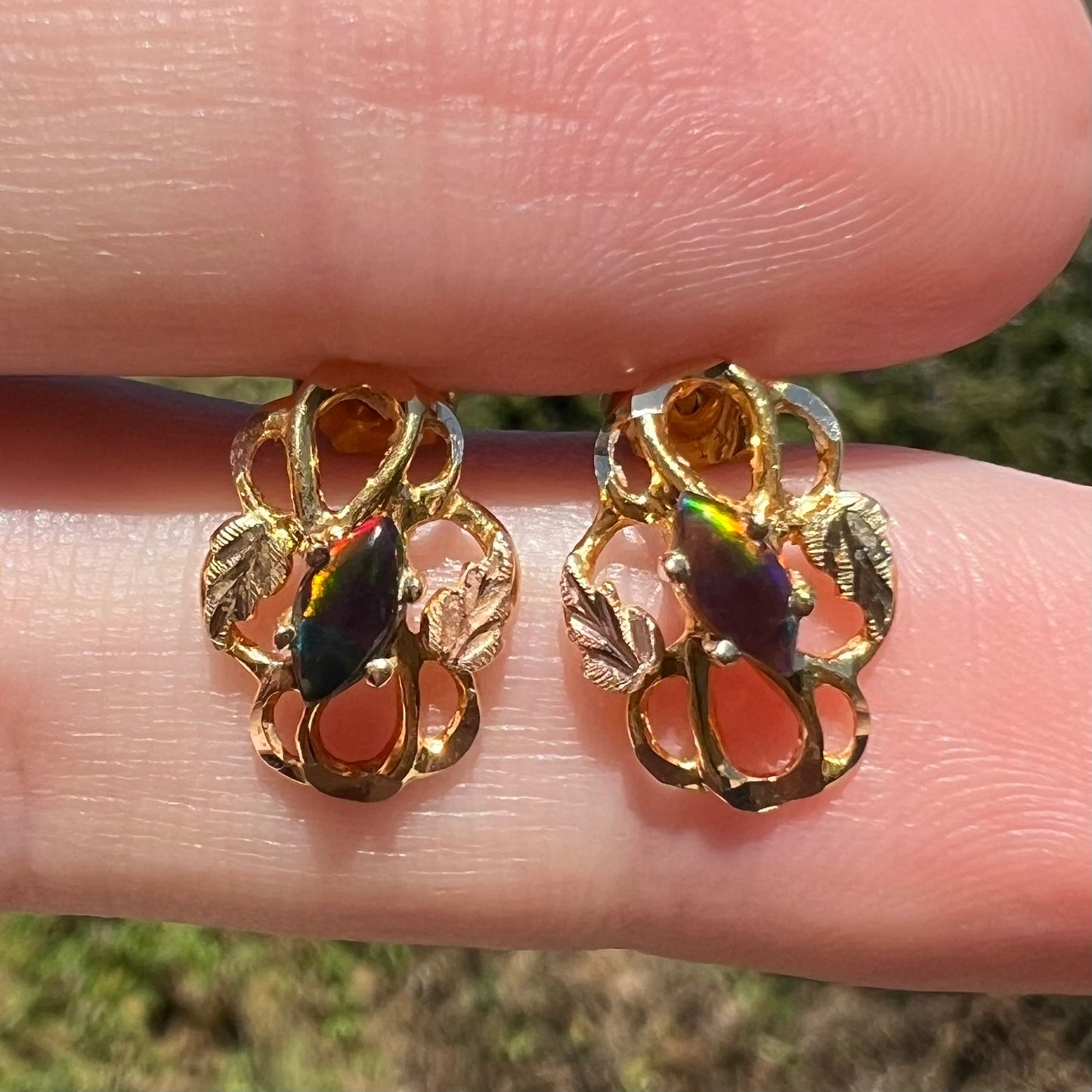Close-up sunlit view of Black hills gold opal earrings, held between fingers