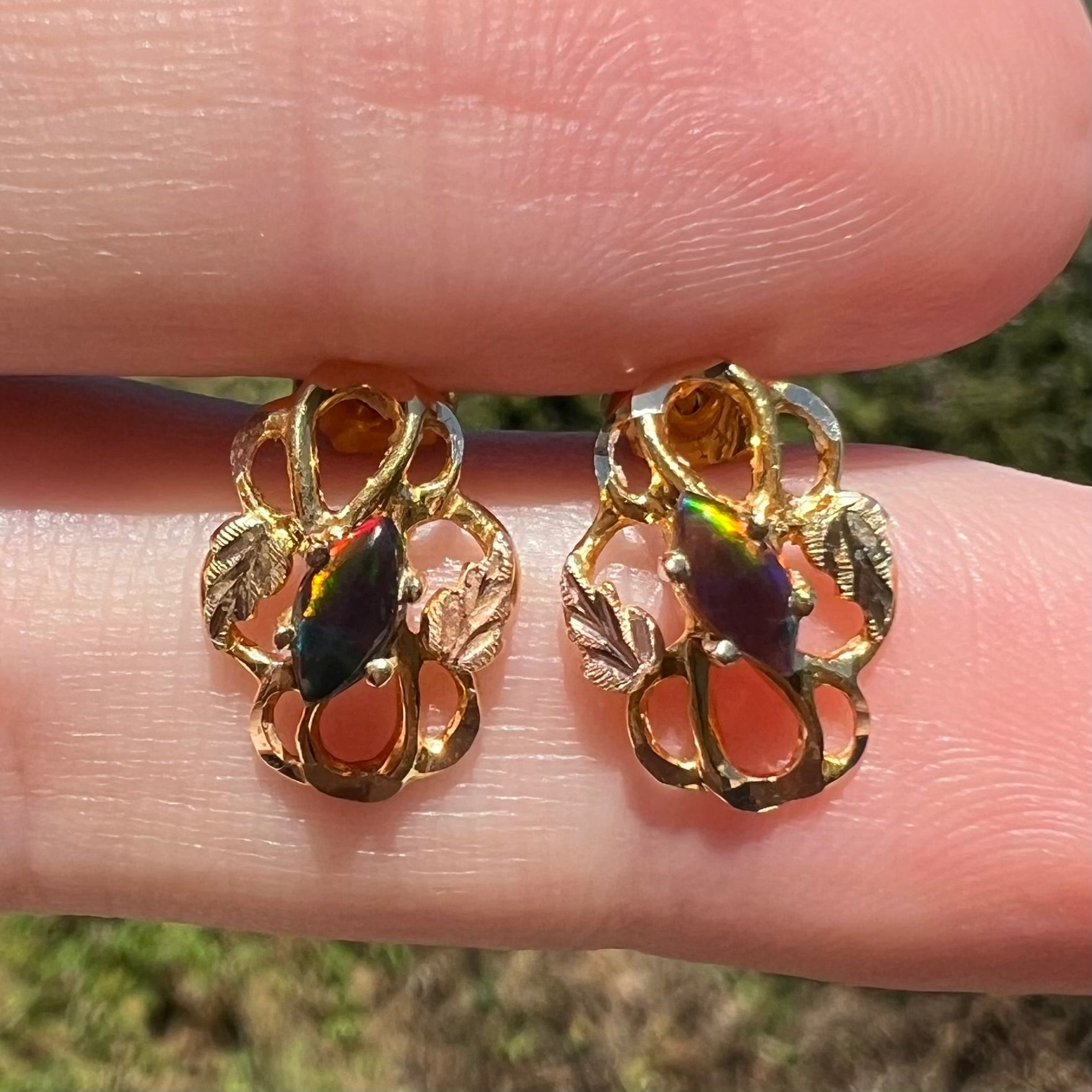 Close-up sunlit view of Black hills gold opal earrings, held between fingers