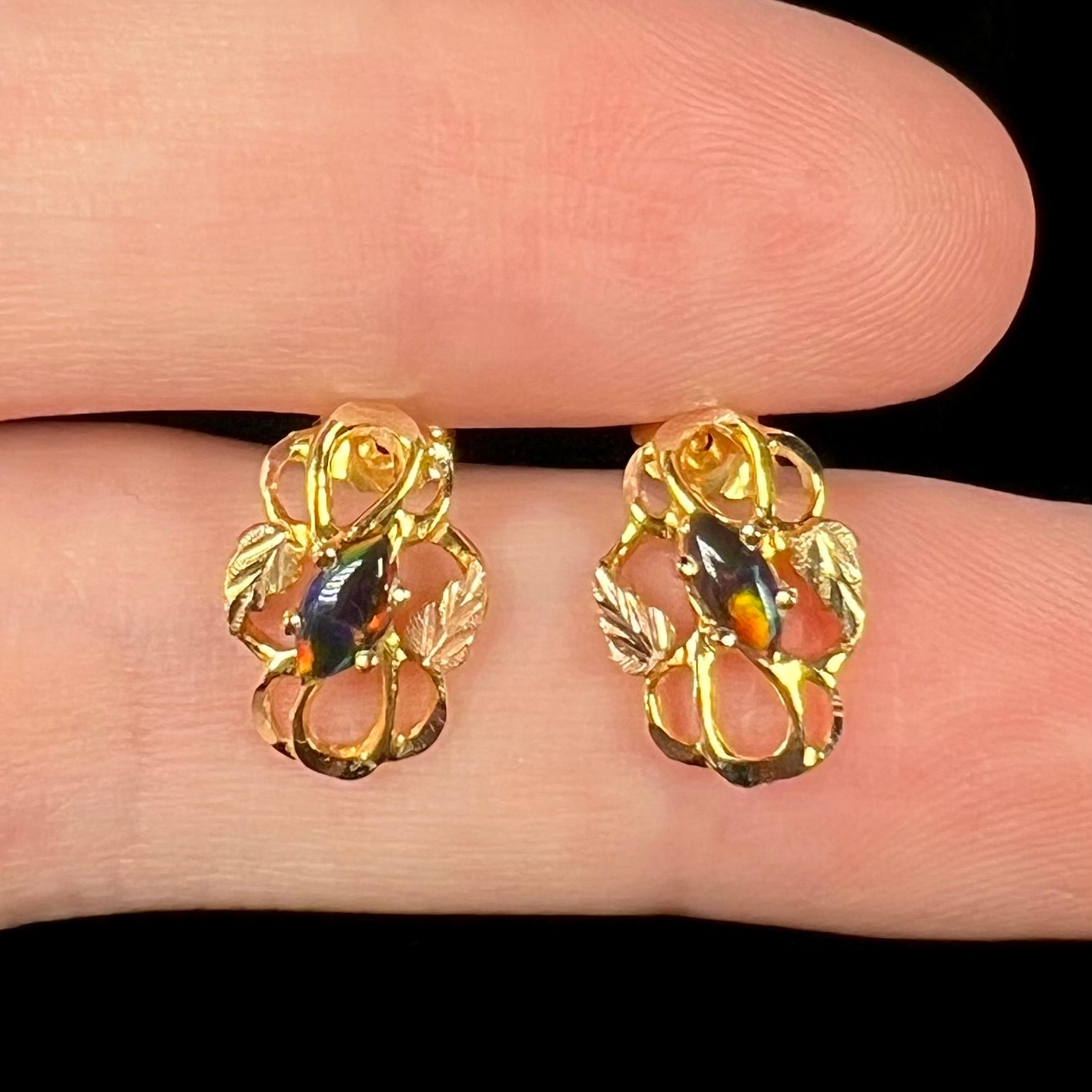 Close-up of Black Hills gold grape leaf design black opal earrings, held in fingers