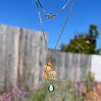 Black Hills gold opal necklace being dangled in a hand outdoors in natural sunlight against a wooden fence.