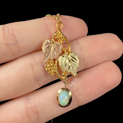 Macro view of a Black Hills gold opal necklace resting on fingers against a black background, highlighting the pendant’s fine details.