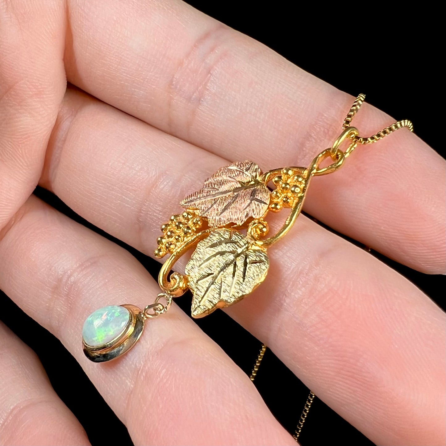 Side-angled view of a Black Hills gold opal necklace against a black background, capturing the opal’s green flashes.