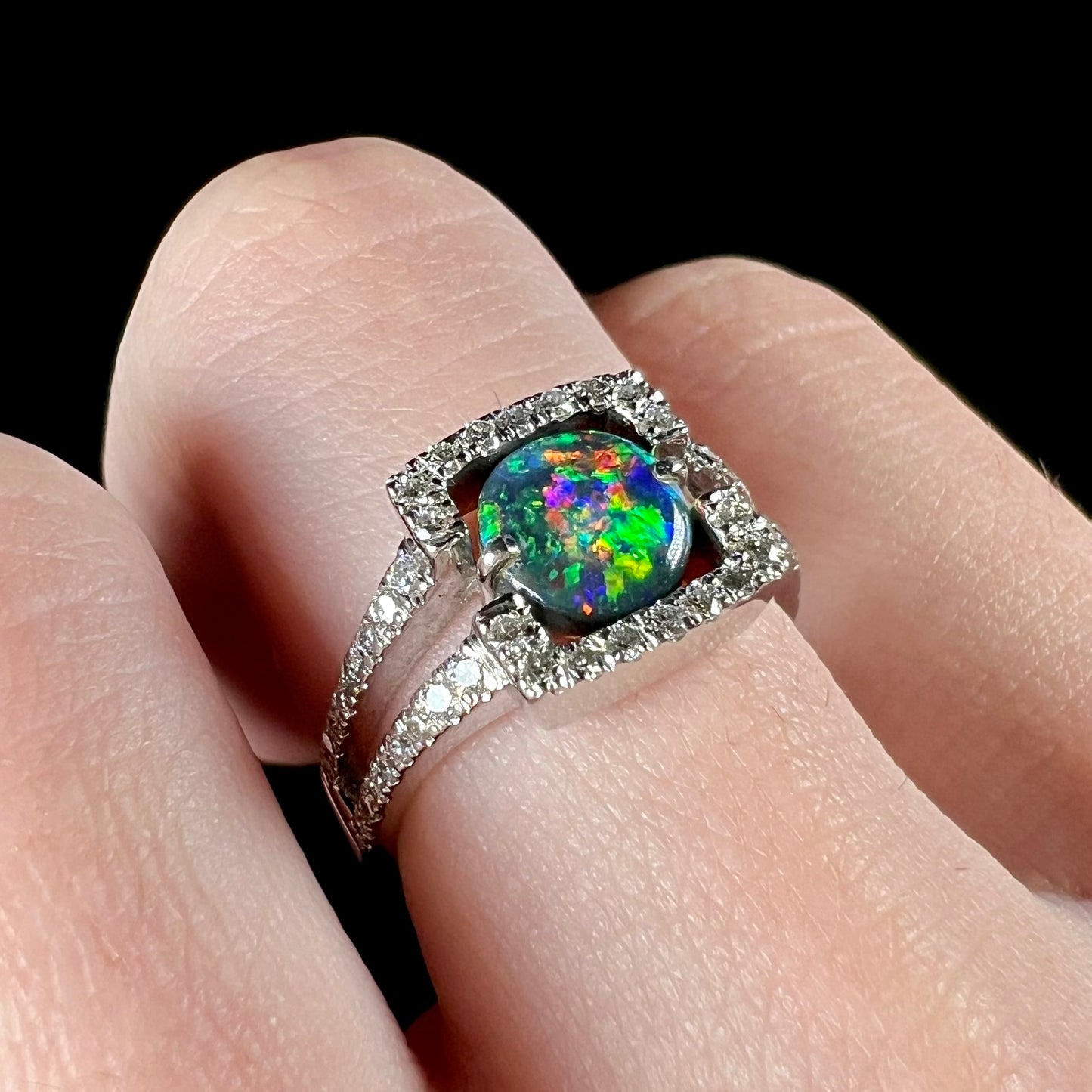 A round black opal and diamond-accented engagement ring in white gold, worn on a hand.