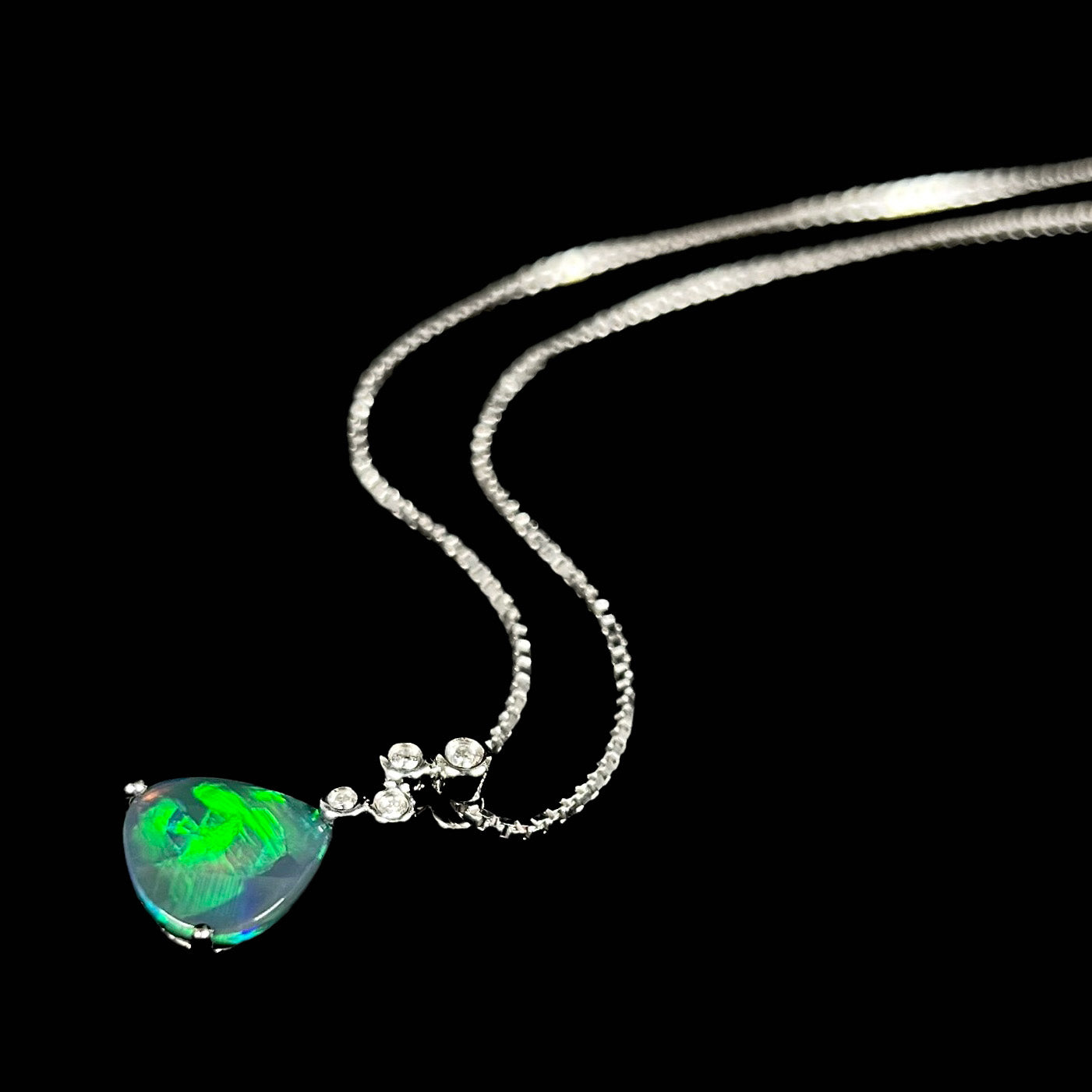 A black opal diamond necklace resting at an angle on a black background, showcasing its directional green flash.