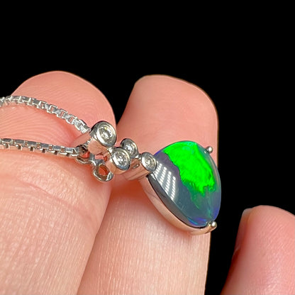 A side-angled macro shot of a black opal and diamond necklace, highlighting a broad green flash.