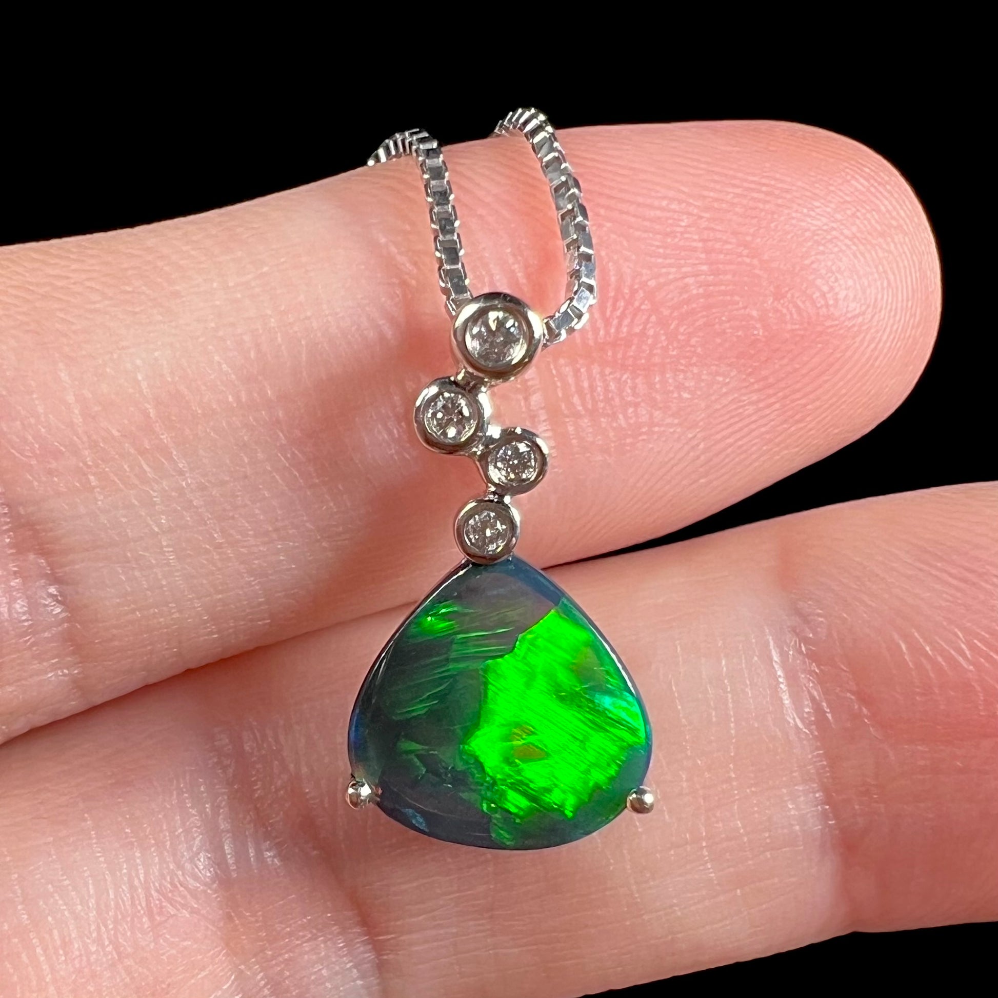 A macro close-up of a black opal and diamond necklace on fingers, showing intricate details of the pendant.