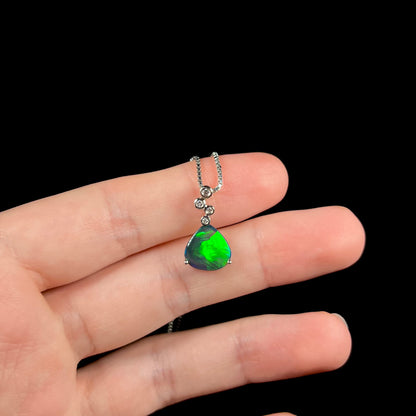 A black opal diamond necklace resting on fingers against a black background, displaying a vivid green flash.