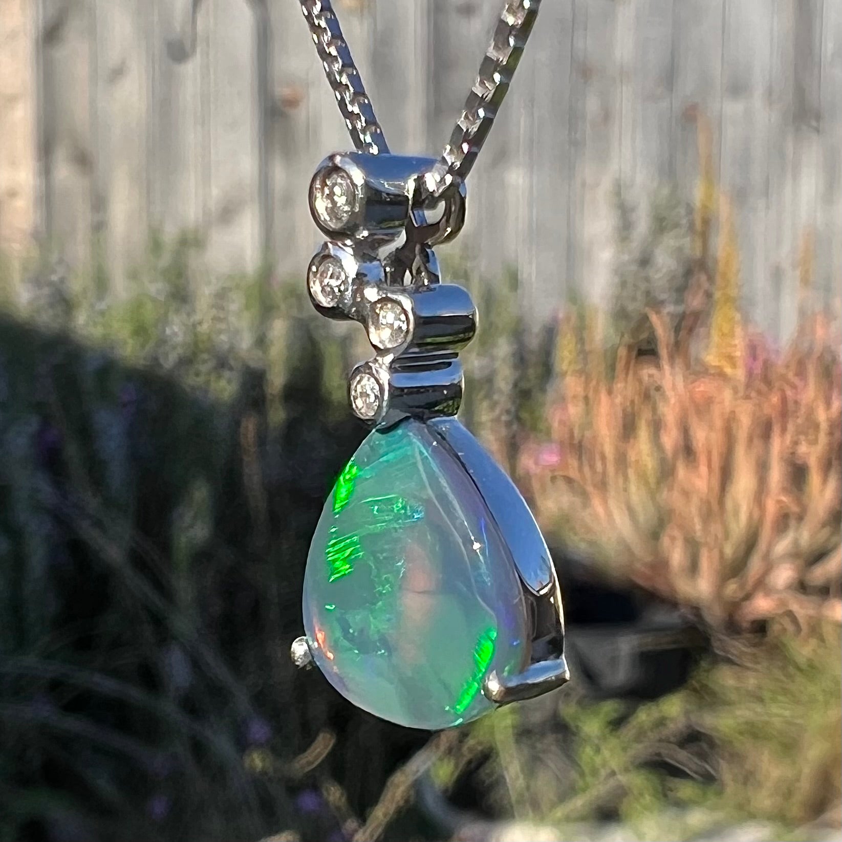 A black opal and diamond necklace at an opposing angle in sunlight, with small areas of green color play visible.