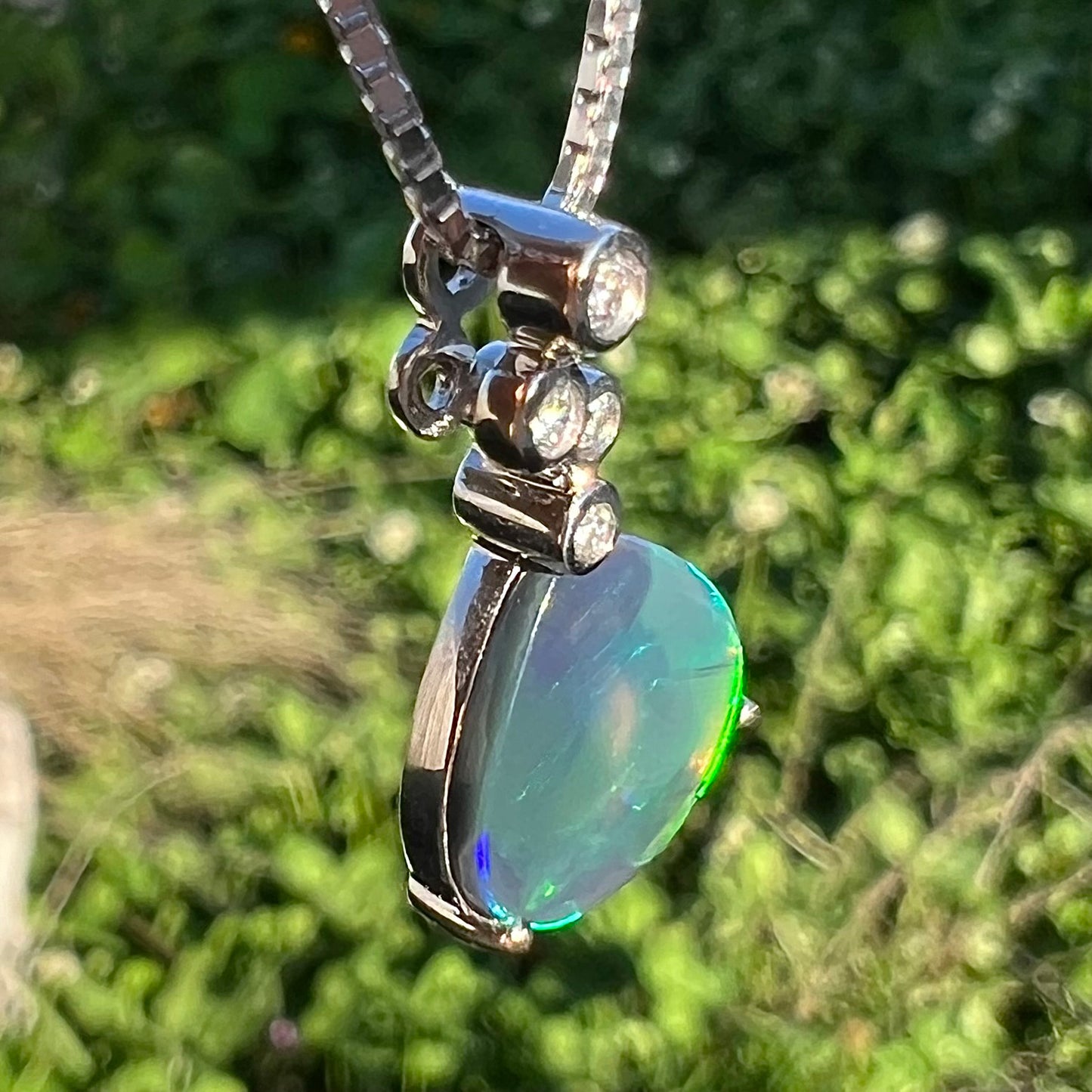 A macro shot of a black opal and diamond necklace at a twisted angle outdoors, showing little to no color play.