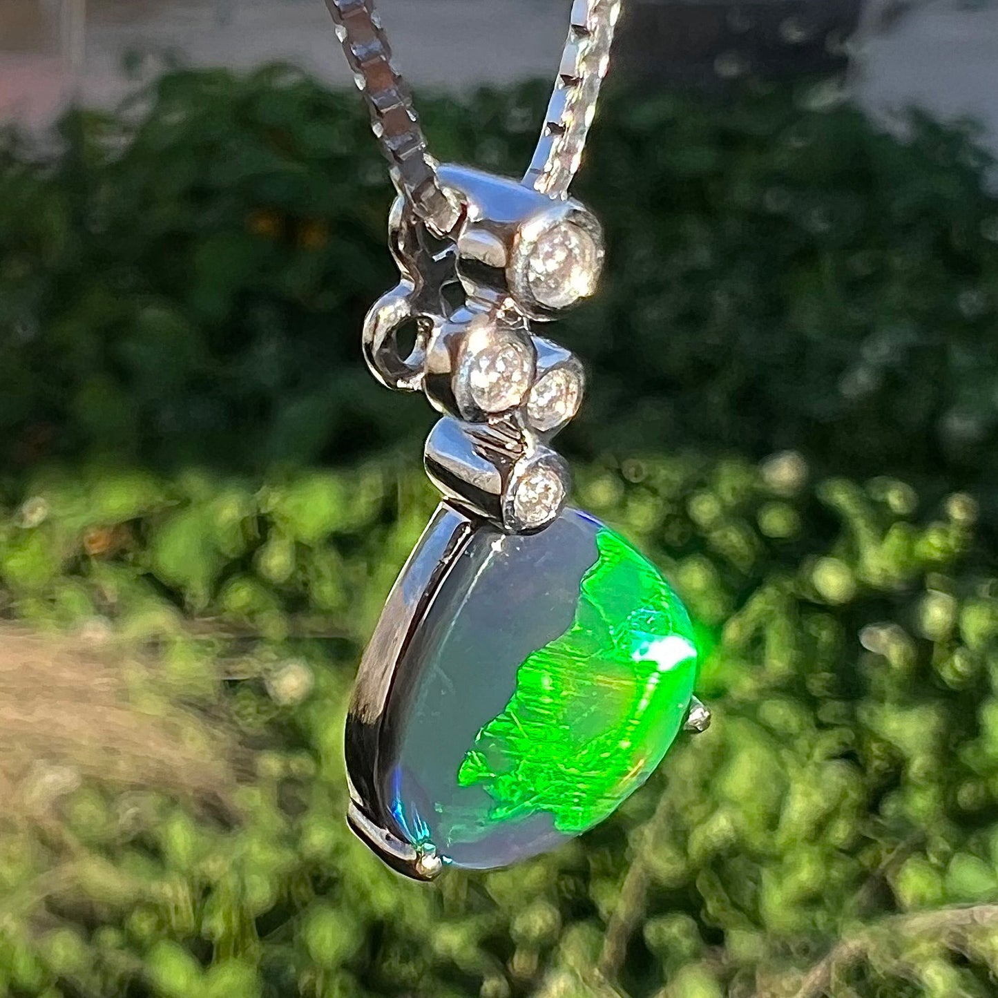 A macro shot of a black opal and diamond necklace at a slight twist in sunlight, revealing a broad green flash.