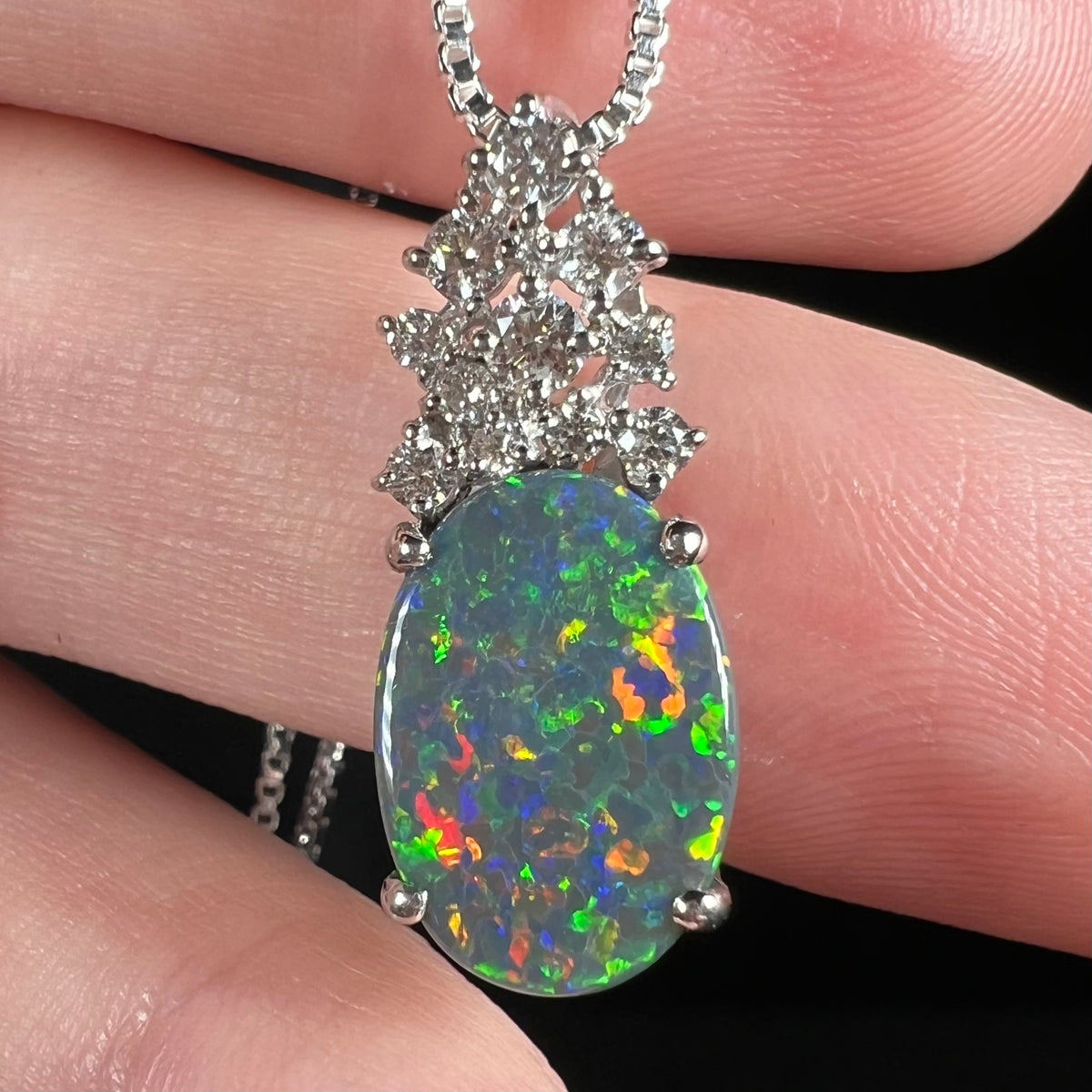 Close-up of Australian black opal and diamond pineapple pendant with multicolor green, orange, red, and blue play-of-color.