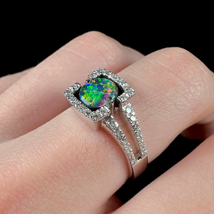 A Lightning Ridge black opal and diamond ring worn on a hand.  The opal shows green color play.