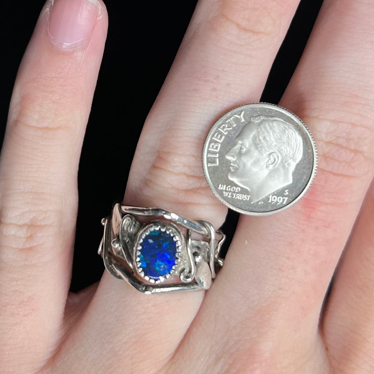Close-up of hand wearing nature-inspired sterling silver black opal doublet solitaire ring next to US dime coin